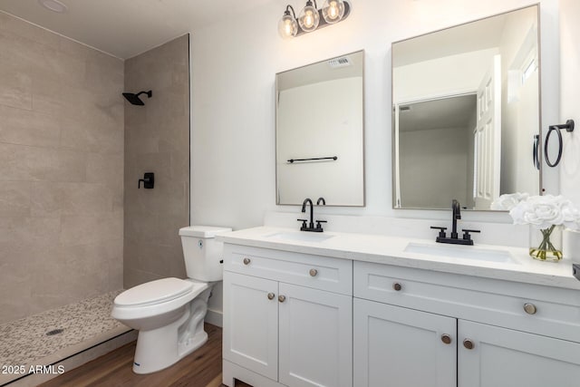 bathroom featuring wood finished floors, toilet, tiled shower, and a sink