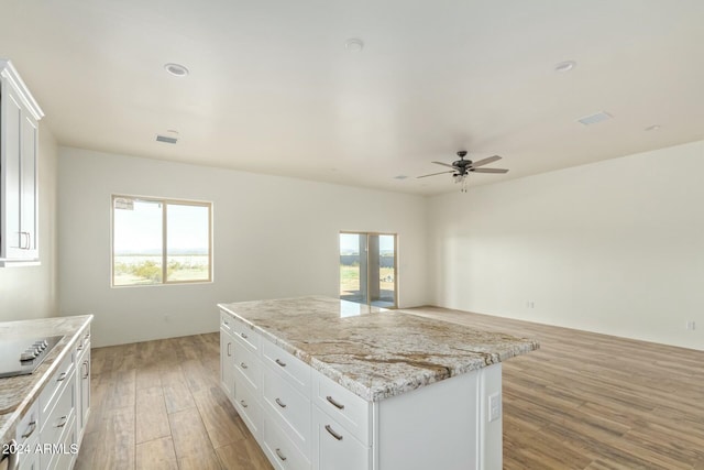 kitchen with white cabinetry, plenty of natural light, light stone countertops, and a kitchen island