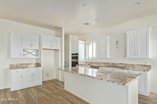 kitchen with white cabinetry, sink, light stone countertops, and a kitchen island