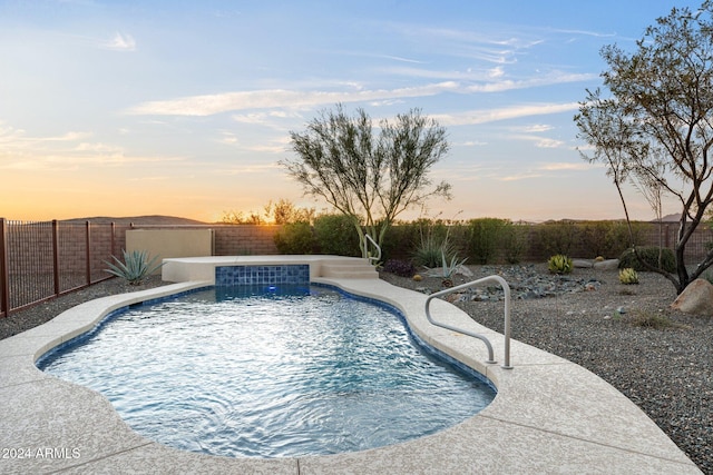 pool at dusk featuring pool water feature and a jacuzzi