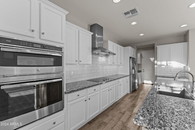 kitchen with white cabinets, appliances with stainless steel finishes, sink, and wall chimney range hood