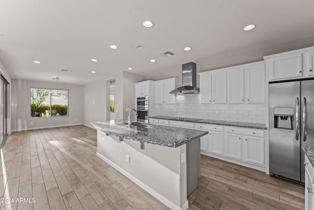 kitchen with dark stone countertops, light wood-type flooring, wall chimney range hood, and appliances with stainless steel finishes