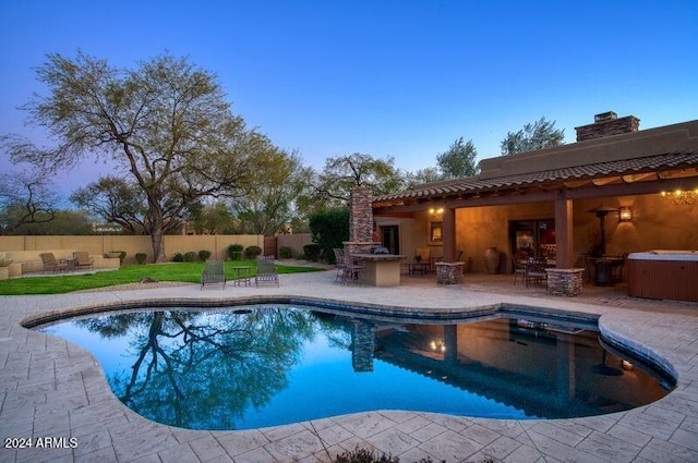 pool at dusk with exterior bar, a patio area, and exterior kitchen