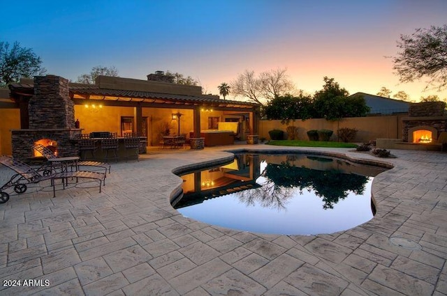 pool at dusk with a patio and an outdoor stone fireplace