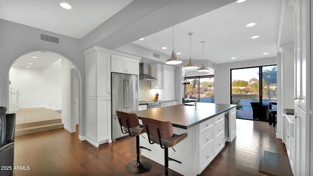 kitchen featuring stainless steel appliances, wall chimney range hood, white cabinets, a center island, and hanging light fixtures