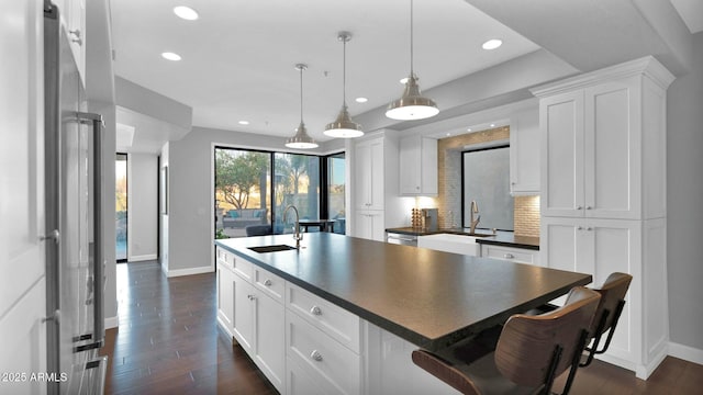 kitchen with white cabinets, decorative light fixtures, a kitchen island with sink, and sink