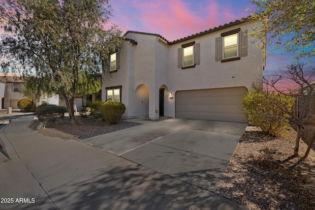 mediterranean / spanish-style home featuring stucco siding, driveway, an attached garage, and a tiled roof