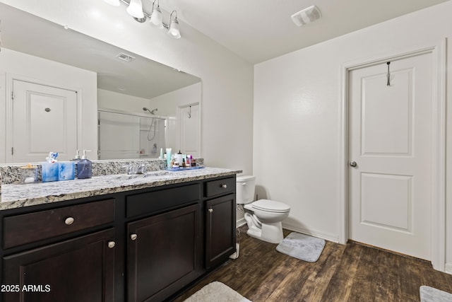 full bath featuring a shower with door, visible vents, toilet, wood finished floors, and vanity
