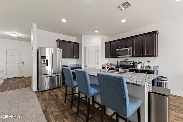 kitchen featuring light stone countertops, visible vents, dark wood-style flooring, dark brown cabinetry, and appliances with stainless steel finishes