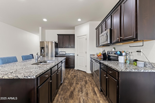 kitchen with a sink, dark wood-style floors, stainless steel appliances, light stone countertops, and dark brown cabinets