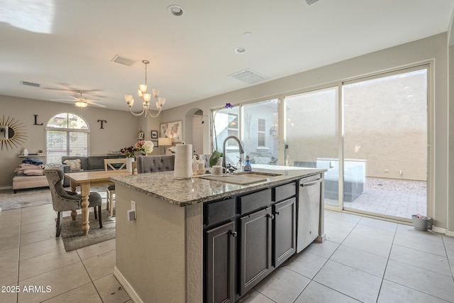 kitchen with decorative light fixtures, dishwasher, light tile patterned floors, light stone counters, and a center island with sink