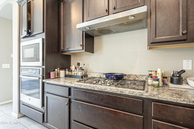 kitchen featuring light stone counters, dark brown cabinetry, stainless steel appliances, and light tile patterned floors