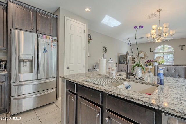 kitchen with pendant lighting, sink, stainless steel fridge, dark brown cabinetry, and light stone countertops