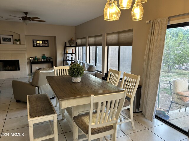 tiled dining area with ceiling fan with notable chandelier and a fireplace