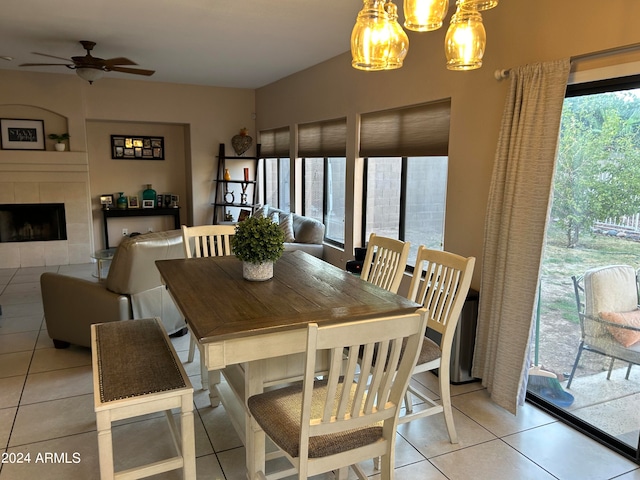 tiled dining space with a tiled fireplace and ceiling fan with notable chandelier