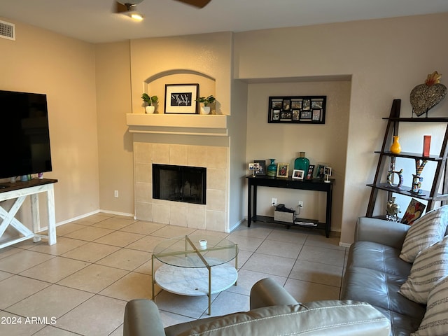 living room with ceiling fan, a tiled fireplace, and light tile patterned flooring