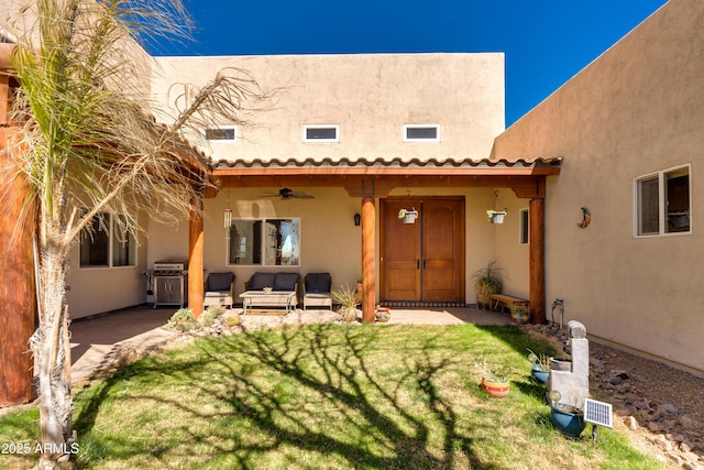 rear view of house with a lawn, a ceiling fan, a patio, and stucco siding