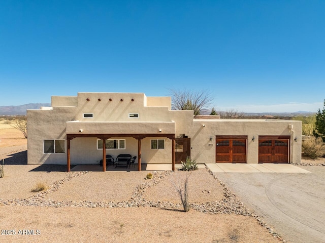 pueblo revival-style home featuring a garage, driveway, and stucco siding