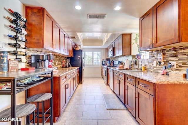 kitchen featuring stainless steel appliances, light stone countertops, sink, and backsplash