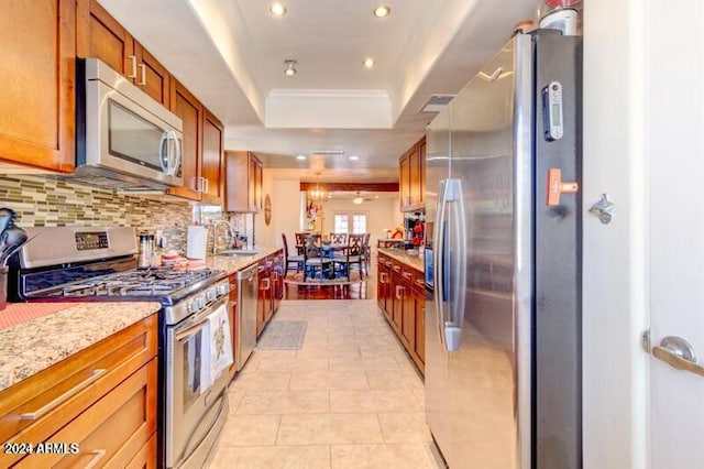 kitchen with stainless steel appliances, backsplash, a raised ceiling, light stone countertops, and sink