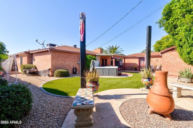 rear view of property featuring a yard, a patio, and a hot tub