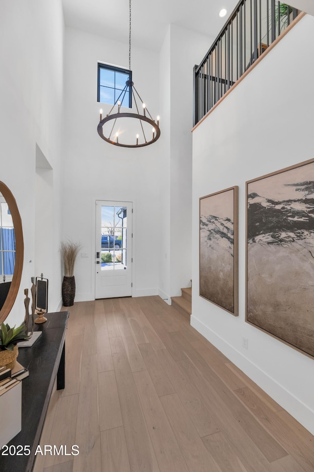 entrance foyer with a towering ceiling, wood-type flooring, and a notable chandelier