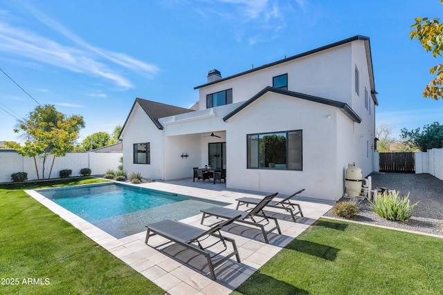 back of property featuring ceiling fan, a patio area, a fenced in pool, and a lawn