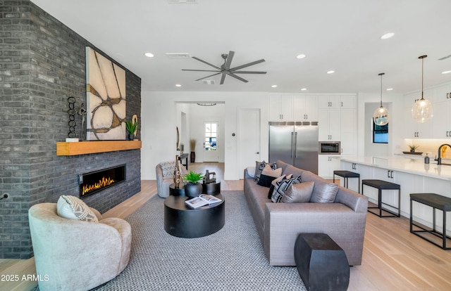 living room featuring ceiling fan, a fireplace, and light hardwood / wood-style flooring