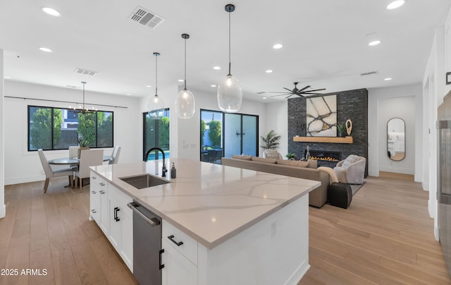 kitchen featuring white cabinetry, an island with sink, a fireplace, light stone counters, and sink