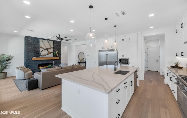 kitchen featuring sink, white cabinets, a center island with sink, and built in appliances