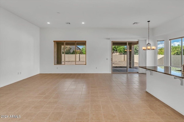 unfurnished living room with an inviting chandelier, plenty of natural light, and light tile patterned floors