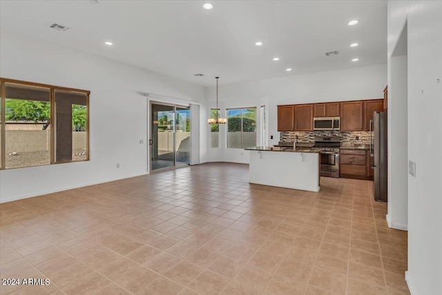 kitchen with an island with sink, light tile patterned floors, decorative light fixtures, appliances with stainless steel finishes, and a kitchen breakfast bar