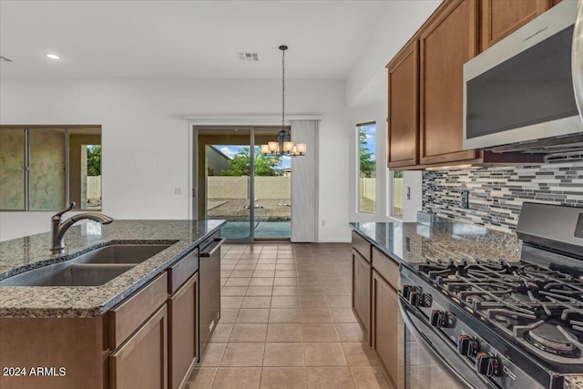 kitchen featuring decorative backsplash, stainless steel appliances, dark stone counters, sink, and a chandelier