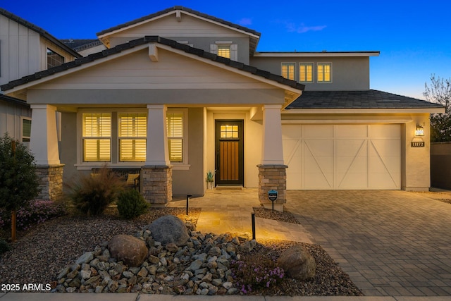 craftsman-style house with a garage, a porch, decorative driveway, and stucco siding