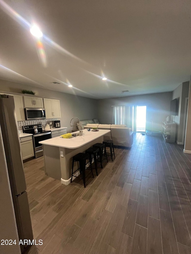 kitchen with dark hardwood / wood-style flooring, sink, a breakfast bar, appliances with stainless steel finishes, and a center island with sink