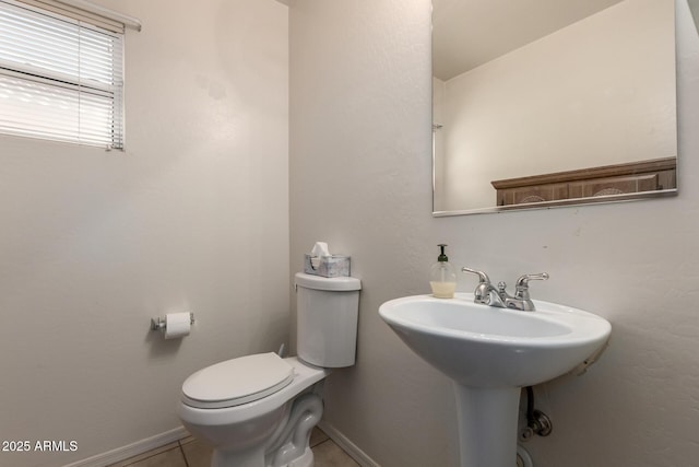 half bath with toilet, tile patterned flooring, baseboards, and a sink