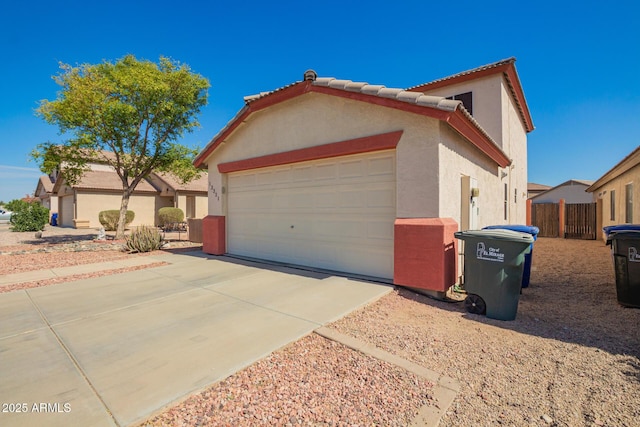 view of side of home featuring a tile roof, stucco siding, concrete driveway, an attached garage, and fence