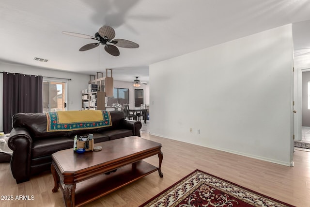 living room with light wood-type flooring, visible vents, and baseboards