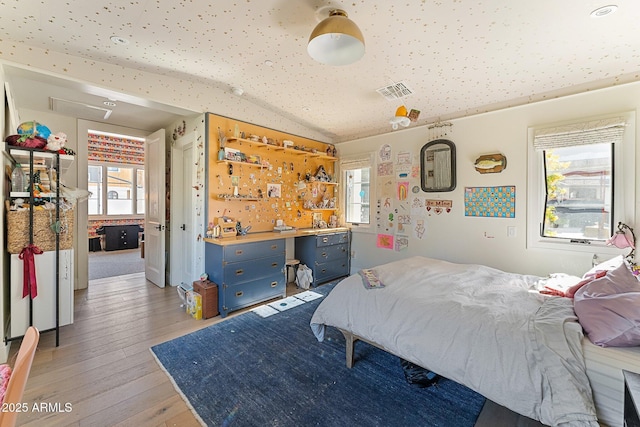 bedroom with multiple windows, light hardwood / wood-style flooring, a workshop area, and vaulted ceiling