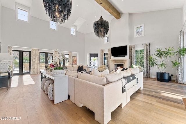 living room with light hardwood / wood-style flooring, an inviting chandelier, beam ceiling, high vaulted ceiling, and french doors