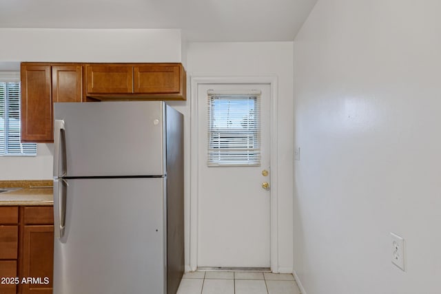 kitchen with light tile patterned floors, light countertops, brown cabinetry, and freestanding refrigerator