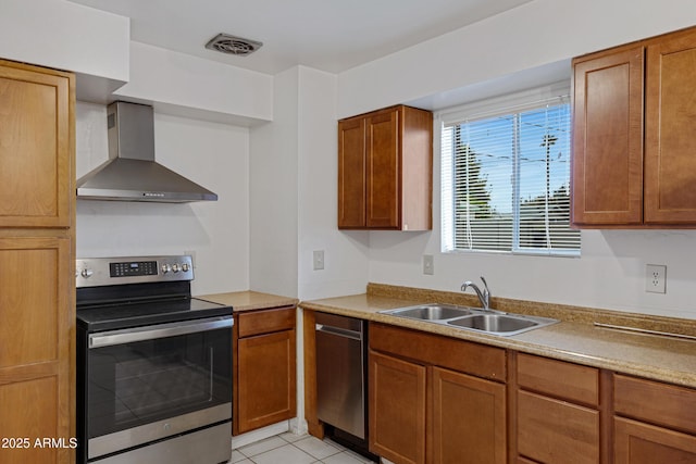 kitchen featuring visible vents, wall chimney range hood, light tile patterned flooring, stainless steel appliances, and a sink