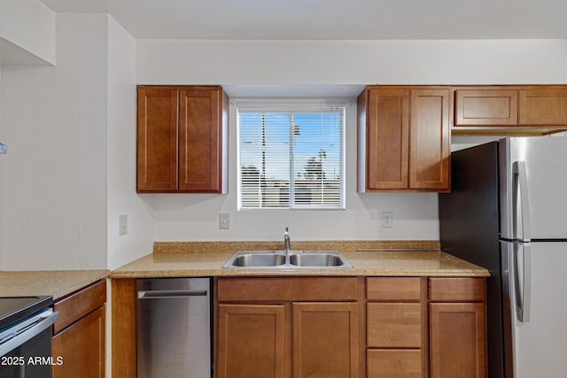 kitchen featuring brown cabinetry, light countertops, freestanding refrigerator, and a sink