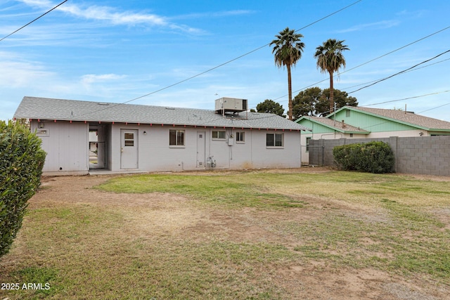 back of property featuring central air condition unit, a lawn, a shingled roof, and fence