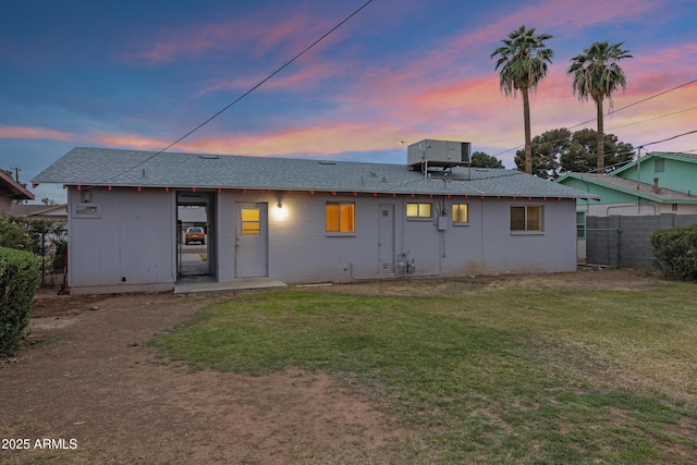 back of property featuring a yard, fence, central AC, and roof with shingles