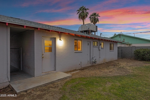 back of house at dusk featuring brick siding, a lawn, and fence