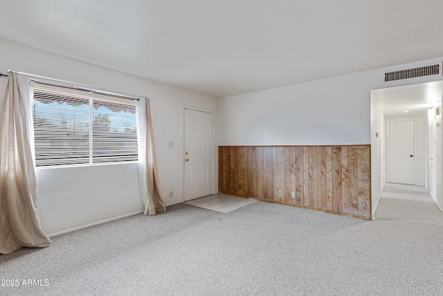 spare room featuring a wainscoted wall, wooden walls, visible vents, and carpet floors