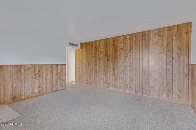 unfurnished room with visible vents, carpet floors, and wood walls