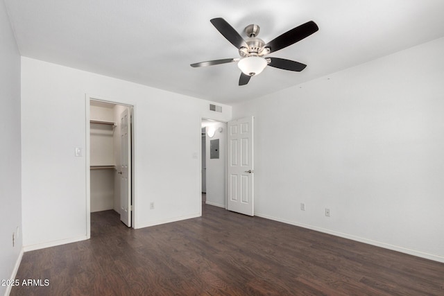 unfurnished bedroom with dark wood finished floors, a spacious closet, baseboards, a ceiling fan, and a closet