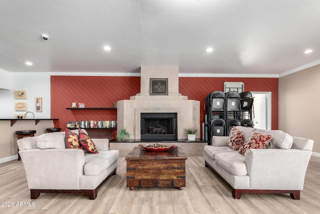 living area with crown molding, an accent wall, baseboards, wood finished floors, and recessed lighting